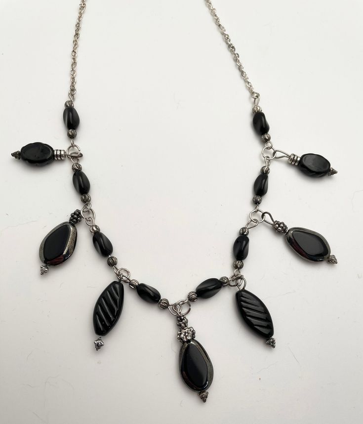 Black, Dark Gray and Silver Necklace and Earrings This necklace is a great basic look, with drops of black.  The drops and beads are all glass.  Along the chain, black slightly twisted glass beads are interspersed.   The drops are all elongated, tear shaped.  The largest are edged in shiny dark silver.  There are also small slightly twisted drops dangling, the same as the black beads interspersed along the chain.  There are medium sized black drops with carving on the sides and larger pressed bl Black Beaded Dangle Jewelry, Black Beaded Chain Dangle Jewelry, Black Beaded Dangle Necklaces, Elegant Black Necklace With Dangling Beads, Black Wire Wrapped Necklace For Party, Black Beaded Dangle Necklace, Black Hematite Beaded Necklaces, Black Beaded Metal Dangle Necklaces, Black Teardrop Metal Jewelry