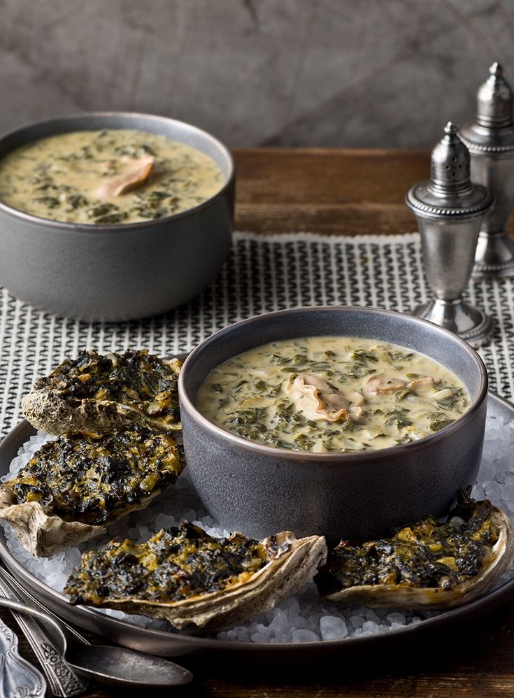 two bowls of soup and some oysters on a plate with silverware next to it