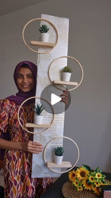 a woman standing next to a tall wooden shelf with potted plants on top of it