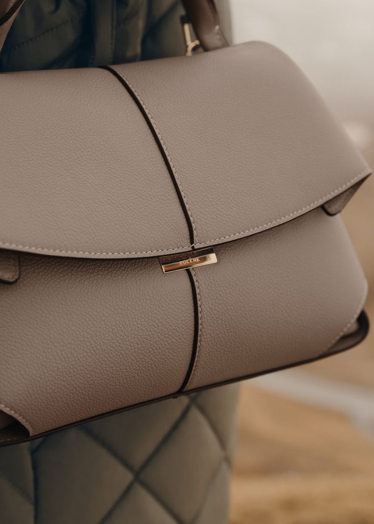 The "Mokki" model showcases the art of folding with its textured leather. The corners are cut to reveal smooth leather for a subtle interplay of textures. The bag’s interior is roomy and divided into compartments, all protected by a flap that features an engraved clasp. With its adjustable shoulder strap held in place by snap hooks, the model smoothly adapts to your movements. Timeless Structured Bag With Smooth Grain, Elegant Textured Leather Flap Bag For Travel, Modern Business Flap Bag With Magnetic Closure, Designer Taupe Top Handle Shoulder Bag, Modern Soft Leather Flap Shoulder Bag, Modern Beige Bags For Everyday Luxury, Modern Flap Bag With Smooth Grain, Modern Structured Bags In Soft Leather, Modern Leather Bag For Everyday Luxury