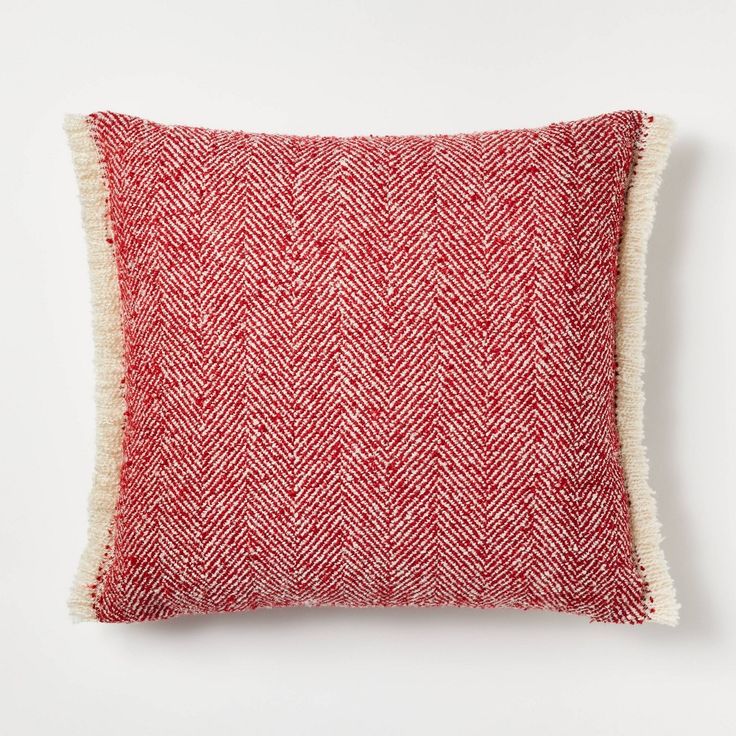 a red and white pillow with fringes on the front, against a white background