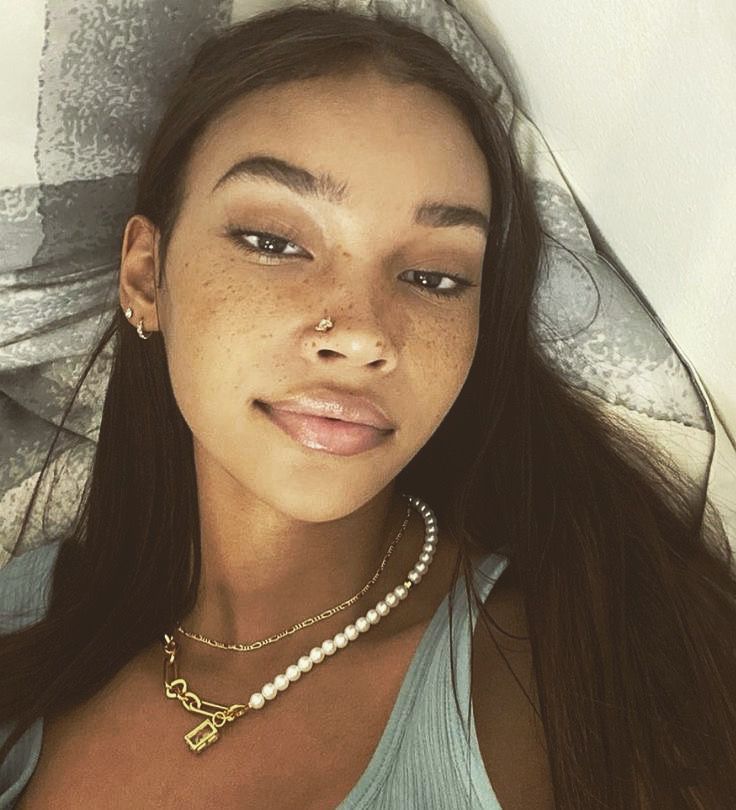 a woman laying on top of a bed wearing a blue shirt and pearl necklaces