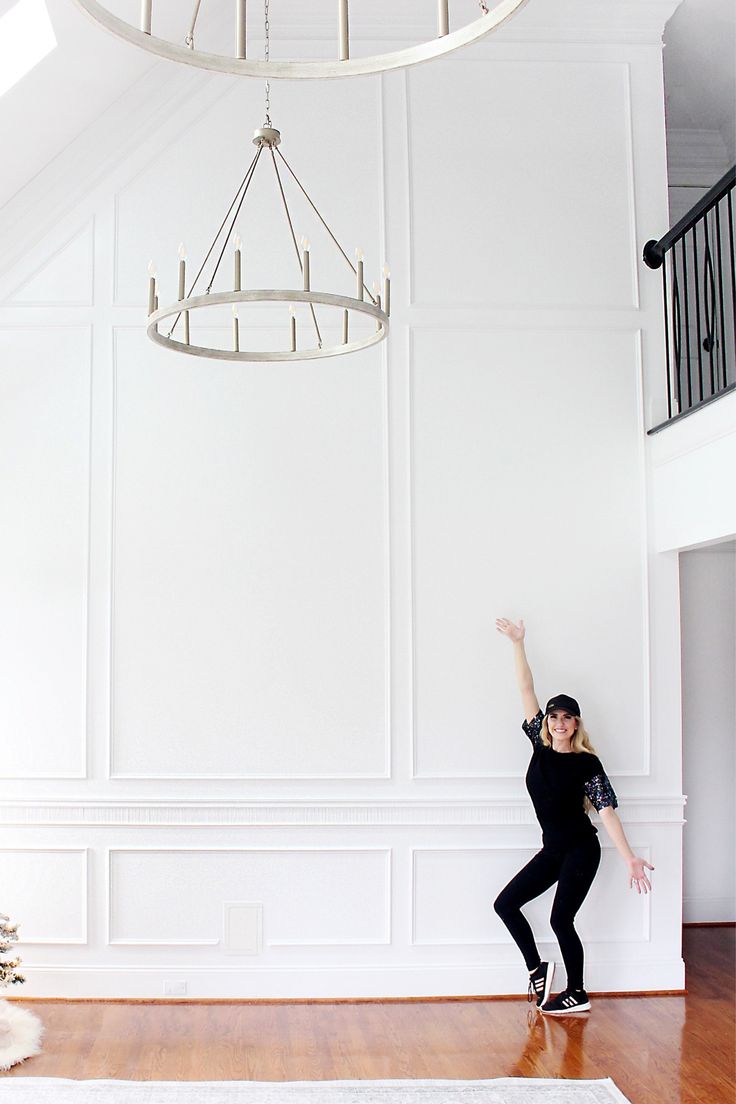 a woman standing in front of a white wall with her arms up and one hand raised