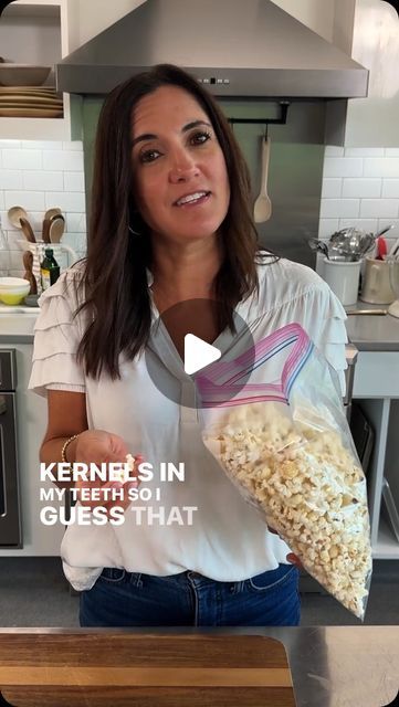 a woman holding a bag of popcorn in her hand while standing next to a counter