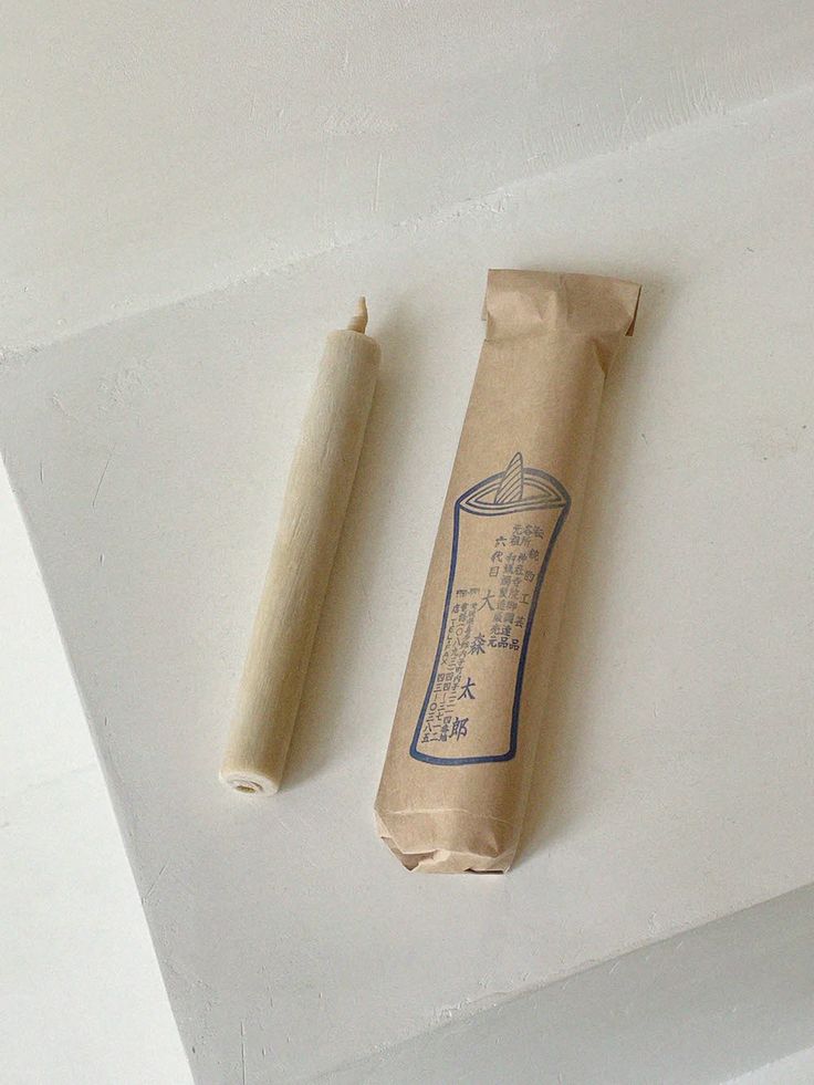 an empty paper bag sitting on top of a white surface next to a rolled up candle