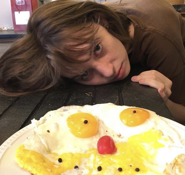 a woman laying her head on a plate with eggs in the shape of a face