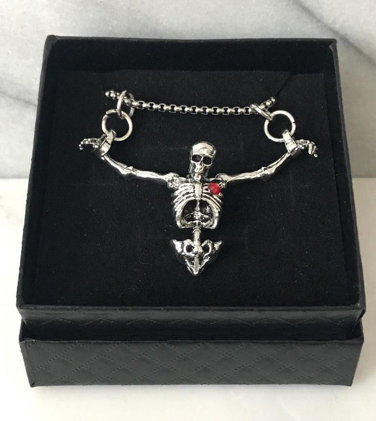 Embrace the darker side of fashion with our Hanging Skeleton Torso Necklace on a stainless steel 18" chain. This unique piece features a silver skeleton hanging from both wrists, adding a touch of Gothic flair to any outfit. You have the option to personalize your necklace by choosing between a skeleton with or without a striking red rhinestone heart accent. The skeleton's head is elegantly tilted forward, enhancing its macabre charm. Perfect for Halloween or as a statement accessory, this neckl Punk Necklace With Lobster Clasp As Gift, Halloween Clavicle Chain Jewelry Gift, Halloween Gift Clavicle Chain Jewelry, Halloween Skull Chain Jewelry, Punk Style Nickel-free Necklace For Gifting, Halloween Stainless Steel Chain Necklace, Punk Heart Pendant Necklace As Gift, Silver Punk Heart Pendant Jewelry, Punk Heart Pendant Necklace For Gift