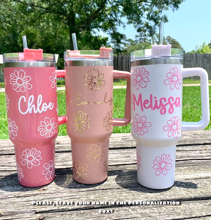 three personalized travel mugs sitting on a picnic table with the name meligo