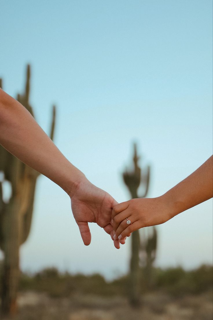 two people holding hands in front of cacti