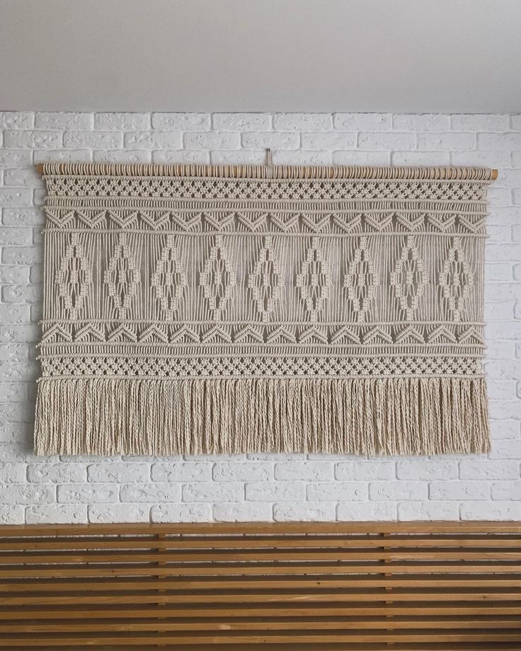 a wall hanging on the side of a white brick wall next to a wooden bench