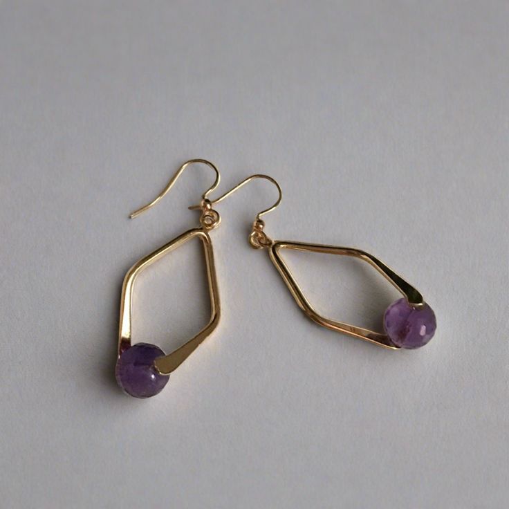 A faceted Amethyst bead set in a double sided diamond shaped frame creates demure drop earrings. 8mm faceted amethyst bead gold plated brass double sided diamond shaped bail gold plated brass french ear wires drop: 2" width: 3/4" Handmade in Lincoln, Nebraska Purple Metal Drop Earrings, Gold Faceted Crystal Earrings For Gift, Purple Teardrop Metal Jewelry, Purple Brass Drop Earrings, Gold Teardrop Faceted Beads Jewelry, Purple Brass Jewelry With Matching Earrings, Gold Teardrop Jewelry With Faceted Beads, Gold Drop Jewelry With Faceted Beads, 14k Gold Filled Faceted Earrings For Gift