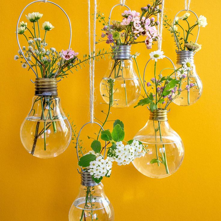 four light bulbs with flowers in them hanging from the ceiling against a bright yellow wall