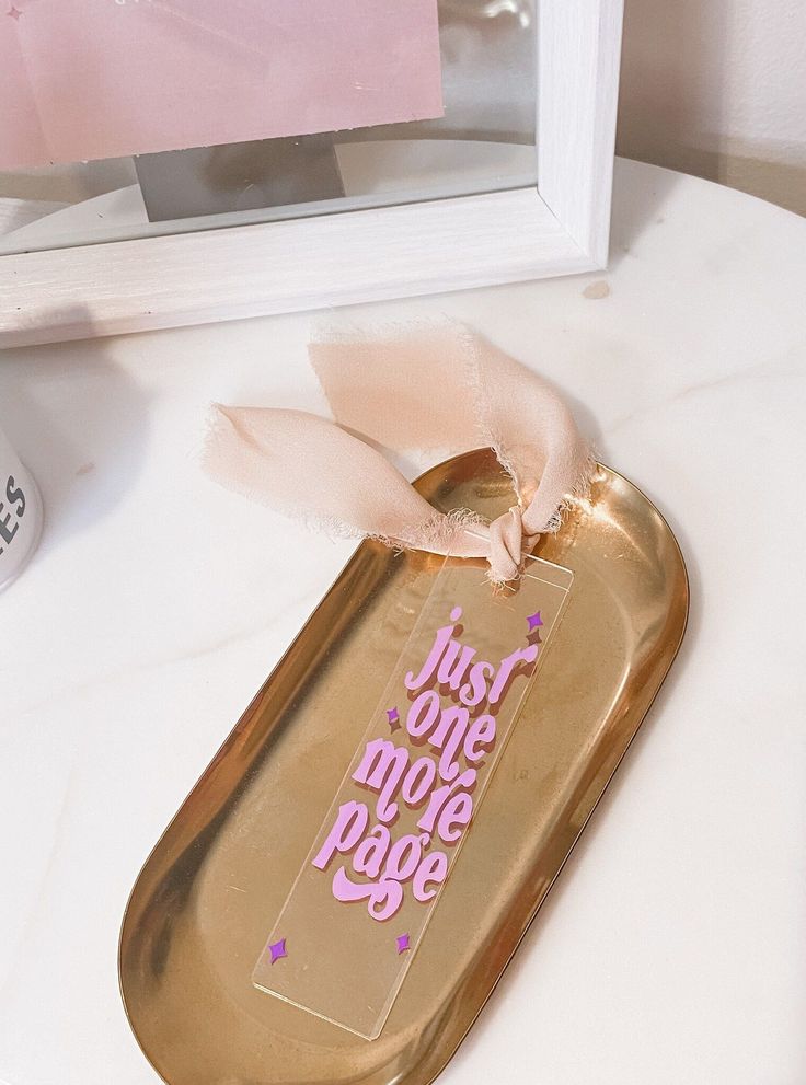 a gold tray with a pink ribbon on it sitting on a table next to a mirror