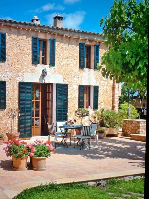 an outdoor patio with potted plants and chairs in front of a stone - colored building