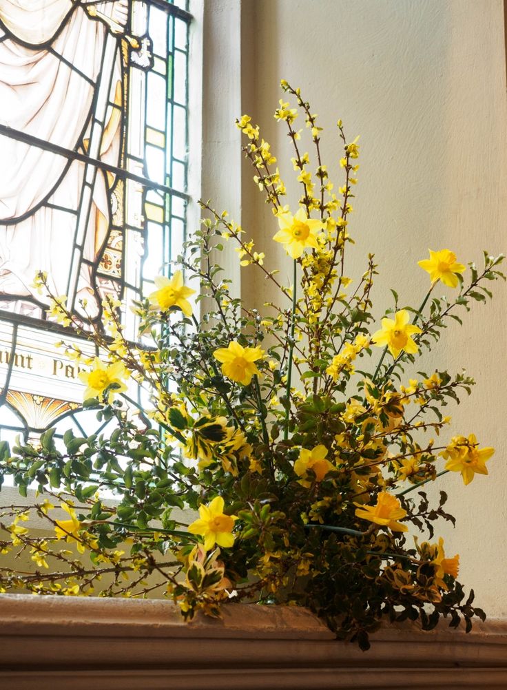 a vase with yellow flowers sitting on top of a mantle next to a stained glass window