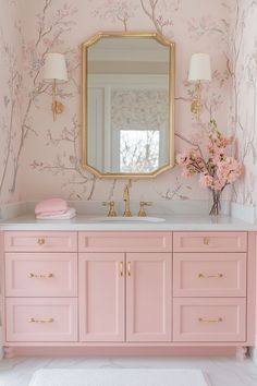 a bathroom with pink and gold decor on the vanity, mirror and flowers in vase