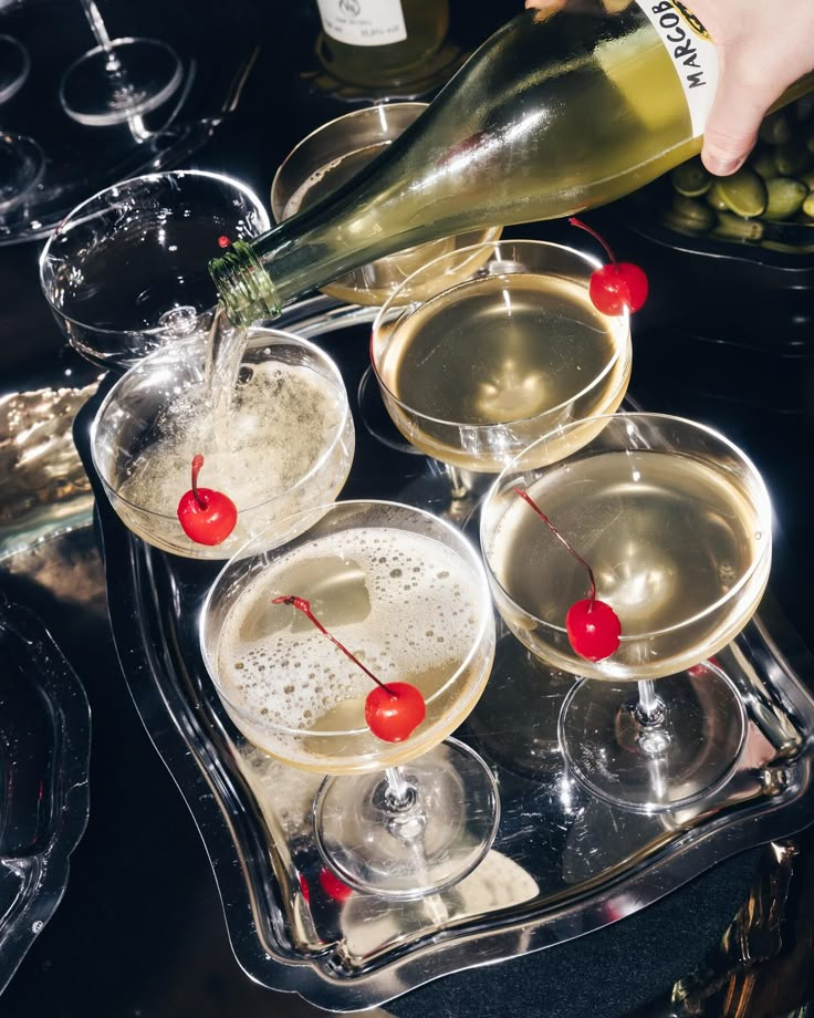 several glasses filled with champagne and cherries on top of a tray next to wine bottles