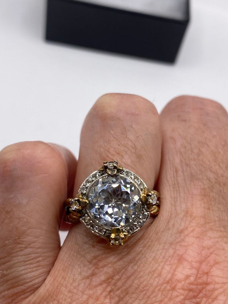 a person's hand holding an engagement ring in front of a black box with a white diamond on it