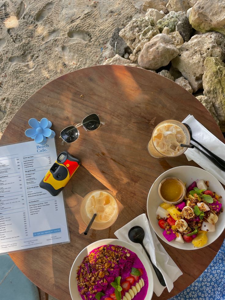 two plates of food on a wooden table next to a menu and glasses with the ocean in the background