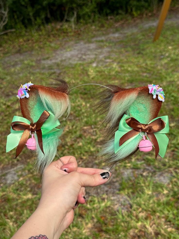 "Mint Chocolate Chip Ice Cream themed Cat ears with detachable bows with pink bells. Mint Green and Brown cat ears topped with white \"frosting\" and sprinkles! (always be gentle handling this style of ears, the sprinkles are delicate!) NOT real sprinkles!  Ears are wired and are posable! Ears come on a metal headband.  My shop's ears and tails are completely hand crafted and might have some slight differences in trimming and airbrushing. Processing times:  Made to order: 4 weeks READY TO SHIP: Cat Ears Outfit, Puppy Boy, Therian Stuff, Mint Chocolate Chip Ice Cream, Cream Cat, Cat Ear Headband, White Frosting, Mint Chocolate Chip, Chocolate Chip Ice Cream