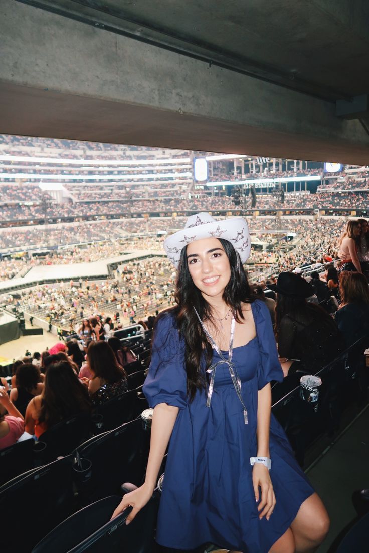 a woman in a blue dress and white hat at a baseball game is posing for the camera