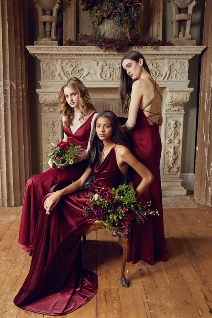 three women in red dresses sitting on a chair with flowers and greenery around them