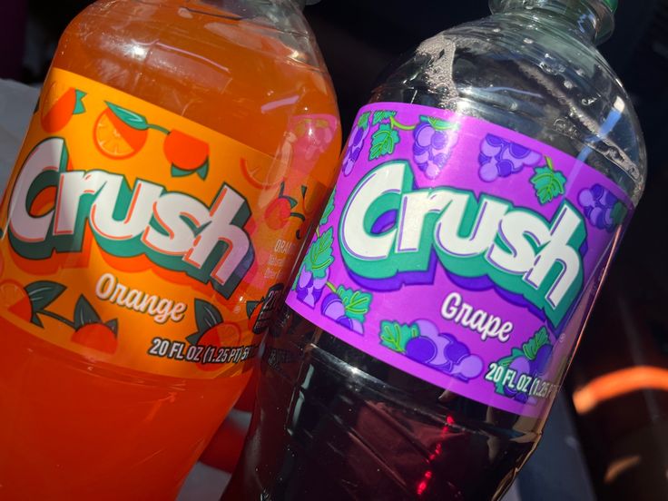 two bottles of crush orange and grape soda sitting next to each other on a table