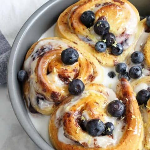 blueberry cinnamon rolls in a pan with icing and fresh blueberries on top