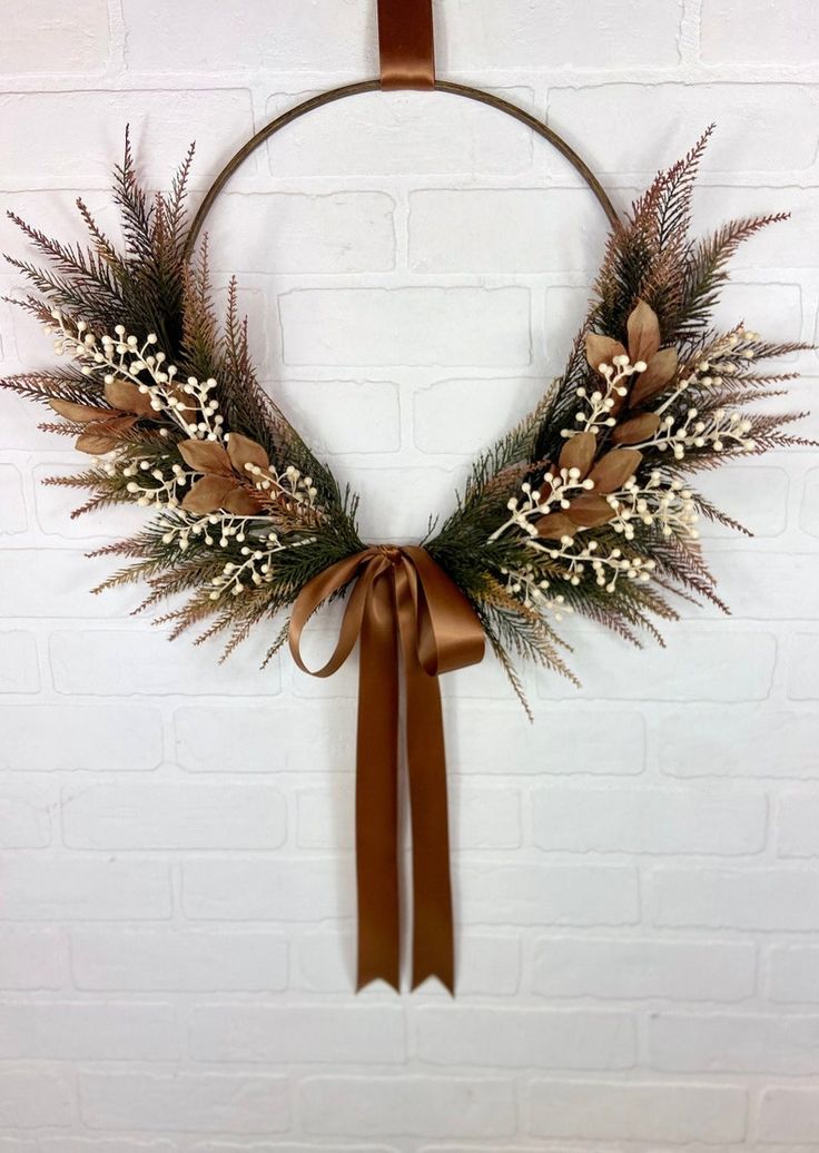 a wreath hanging on a brick wall with a brown ribbon and some white flowers in it