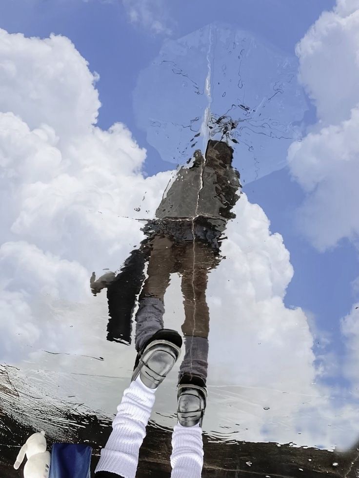 the reflection of a person standing on a skateboard in water with clouds and blue sky