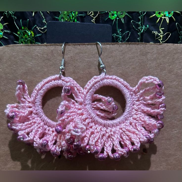 pink crochet earrings with silver hooks on brown box outside in front of green plants