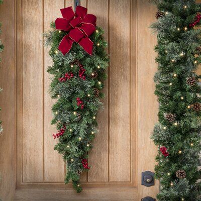 two christmas wreaths hanging on the front door with red bows and lights around them