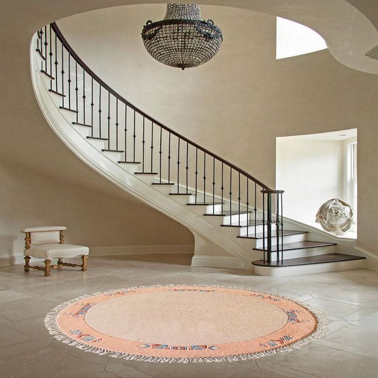 a circular rug on the floor in front of a stair case and chandelier