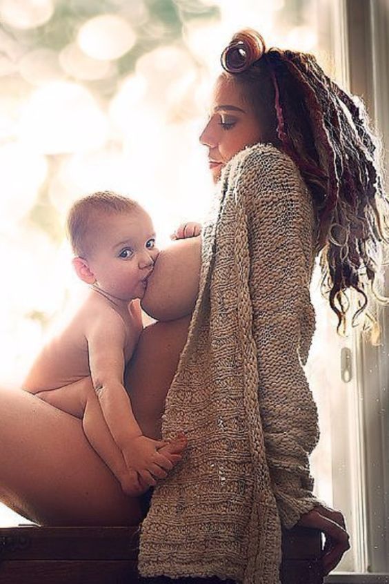 a woman holding a baby in her lap while sitting next to a window sill