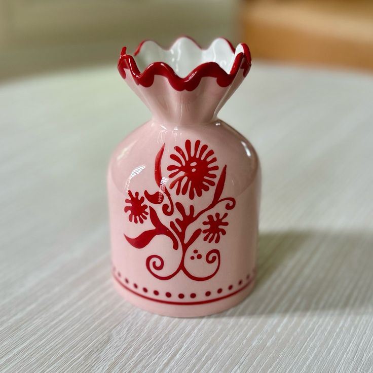 a pink vase with red designs on it sitting on top of a white tablecloth