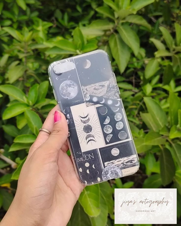 a woman holding up her phone case with the moon and stars on it in front of some bushes