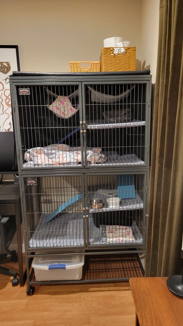 a metal cage filled with baby blankets on top of a wooden desk next to a window