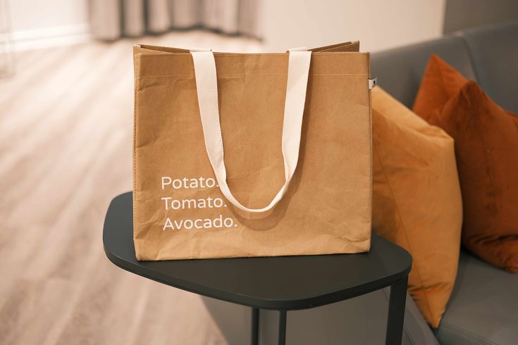 a brown paper bag sitting on top of a table next to a gray couch and pillows