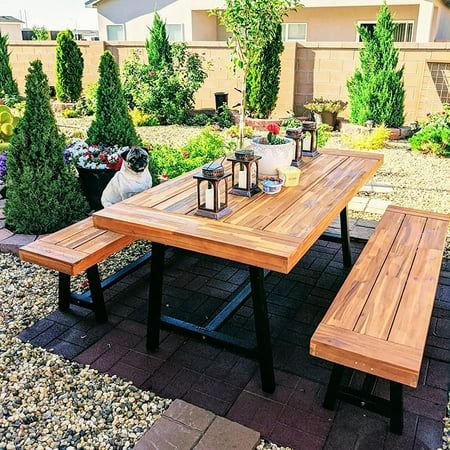 a wooden table sitting on top of a brick patio next to potted plants and trees