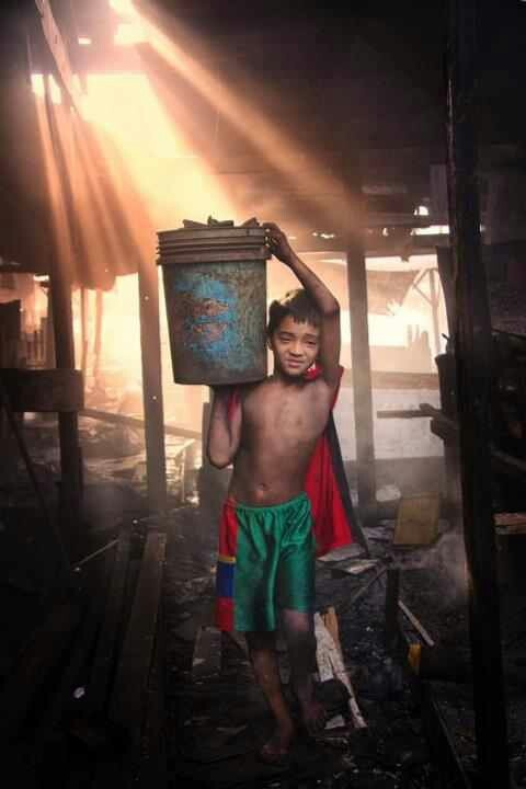 a young boy carrying a bucket on his head while standing in a burned out building