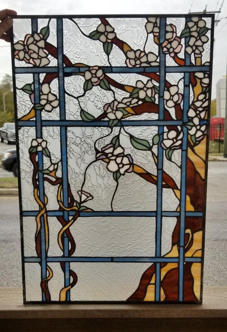 a stained glass window with white flowers and leaves on it, in front of a street