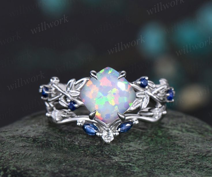 an opal and blue sapphire ring on top of a rock with leaves around it