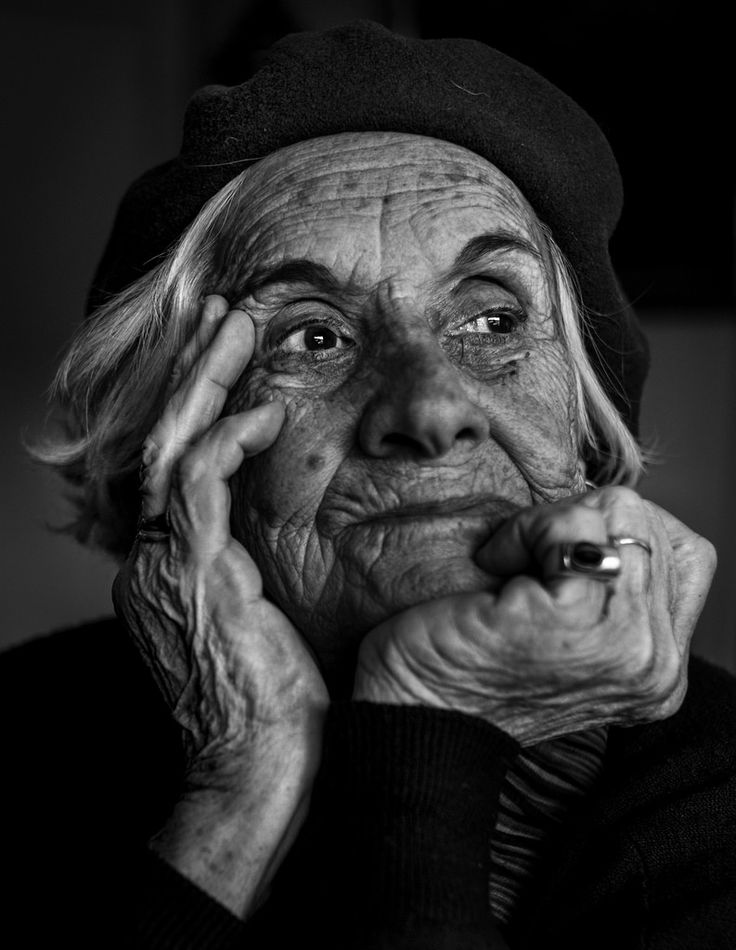 an old woman with wrinkles holding her hand to her face and looking at the camera