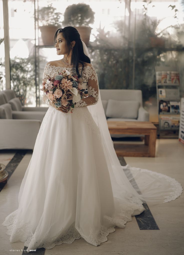 a woman in a wedding dress holding a bouquet and looking at the camera while standing in front of a couch