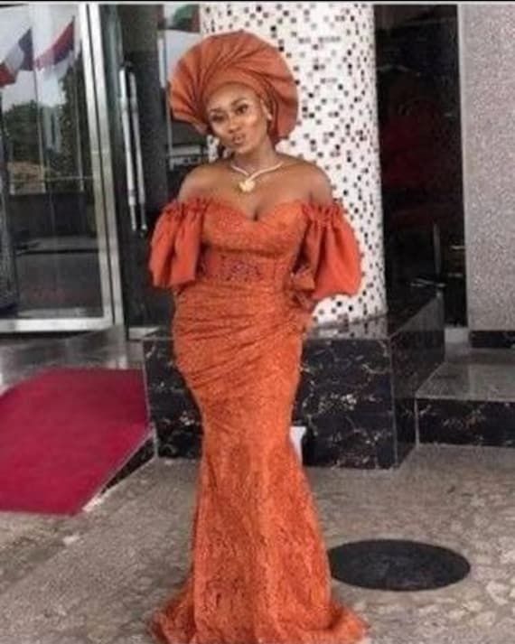 This Off Shoulder dress is perfect for any Nigerian wedding, or special occasion. The dress is made of high quality African lace and is designed to make a statement. The off-shoulder style gives the dress a unique look that is sure to turn heads. The traditional design will make you feel like royalty at your next event. The burnt orange color is perfect for any Nigerian wedding, especially if you want to stand out. As a wedding guest, bridesmaid, or dinner date, this dress is sure to make you feel special and beautiful. The dress features a flattering fit and a comfortable feel so you can enjoy your day without worrying about being uncomfortable. No matter the occasion, this Off Shoulder dress is perfect for a special day. Note: Please note that the exact fabric might not be available as a Nigerian Lace Dress, Aso Ebi Lace, Aso Ebi Lace Styles, African Bridal Dress, Nigerian Lace Styles, Ankara Short Gown Styles, African Lace Styles, Lace Gown Styles, Lace Dress Styles