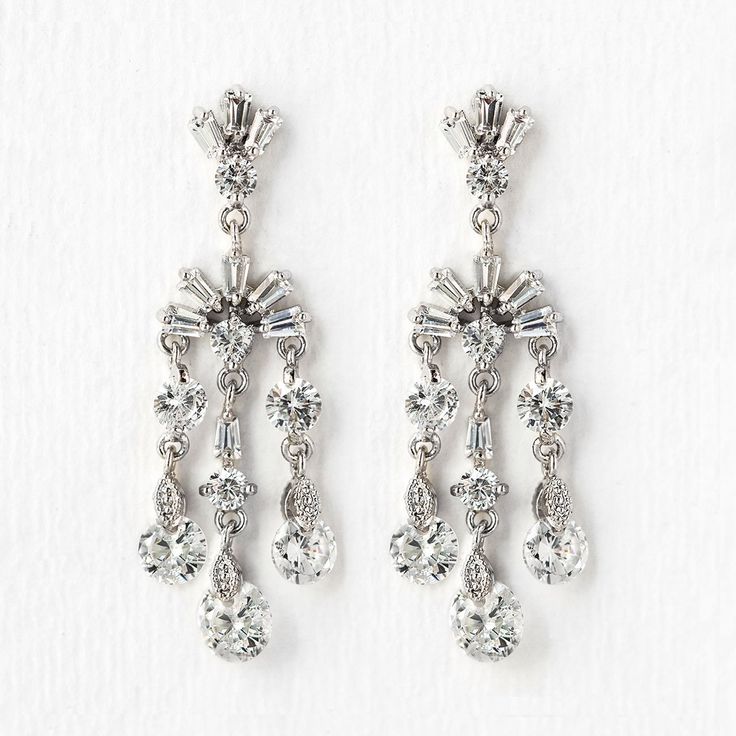 two pairs of earrings with crystal stones on them, one is dangling from the side