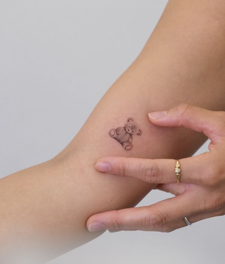 a small tattoo on the arm of a woman with a teddy bear drawn on it