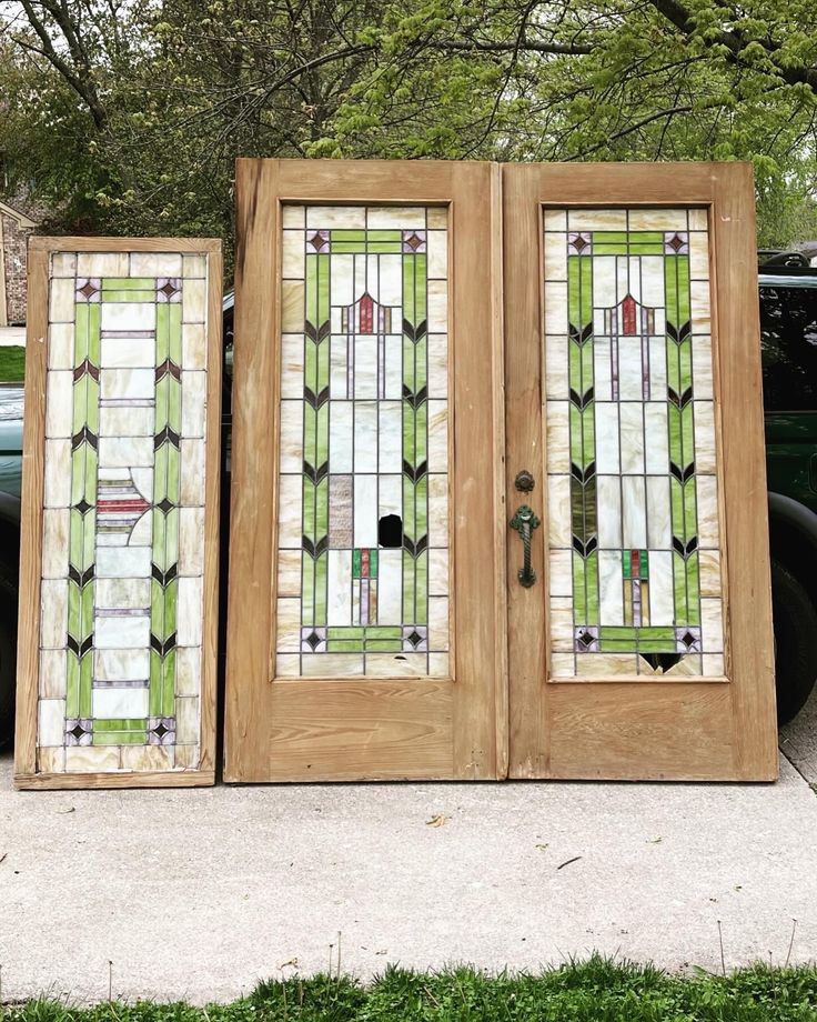 two stained glass doors sitting on the side of a sidewalk next to a car in front of a tree