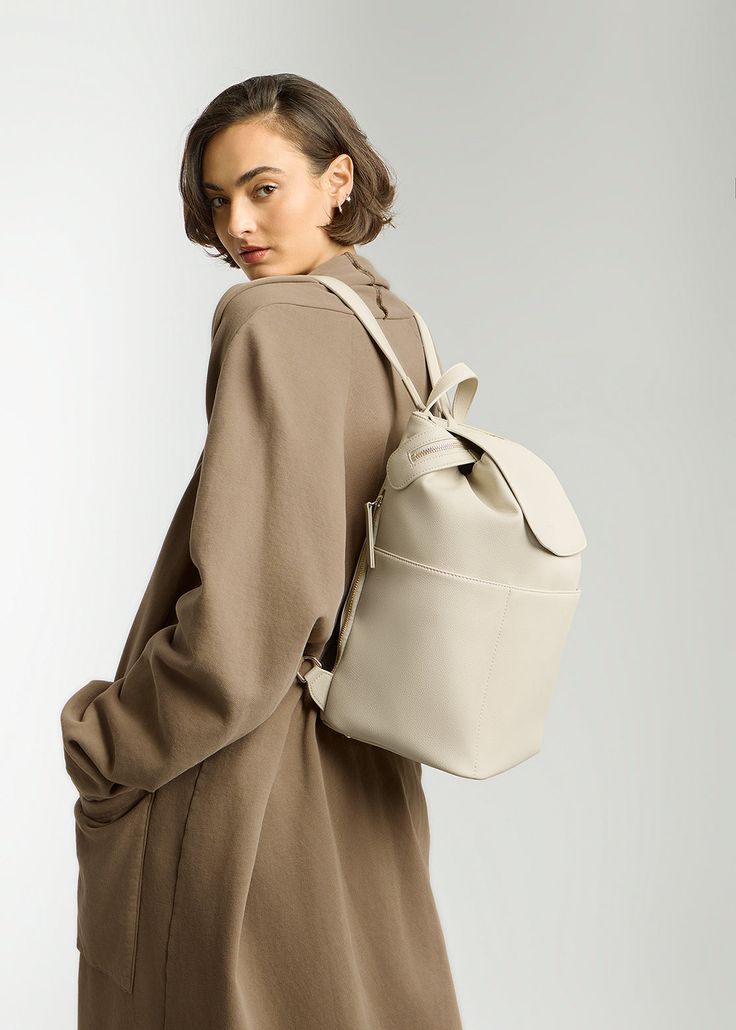 a woman in a brown coat carrying a white backpack