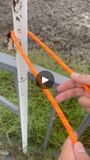 someone is tying an orange string to a metal fence post with two hands and one hand